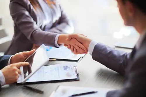 Two business people shaking hands over financial documents